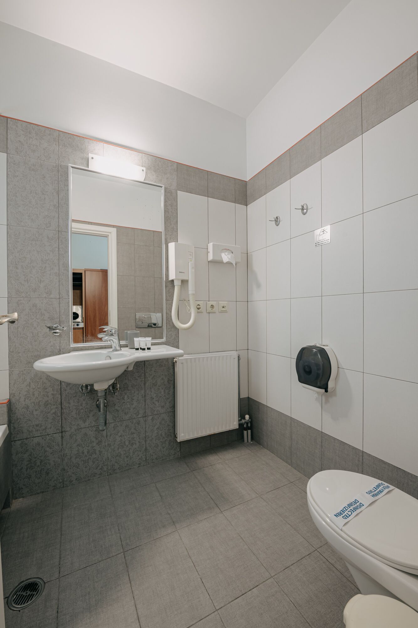 Une salle de bain moderne équipée d’un lavabo, d’un miroir, de toilettes et d’un sèche-mains.