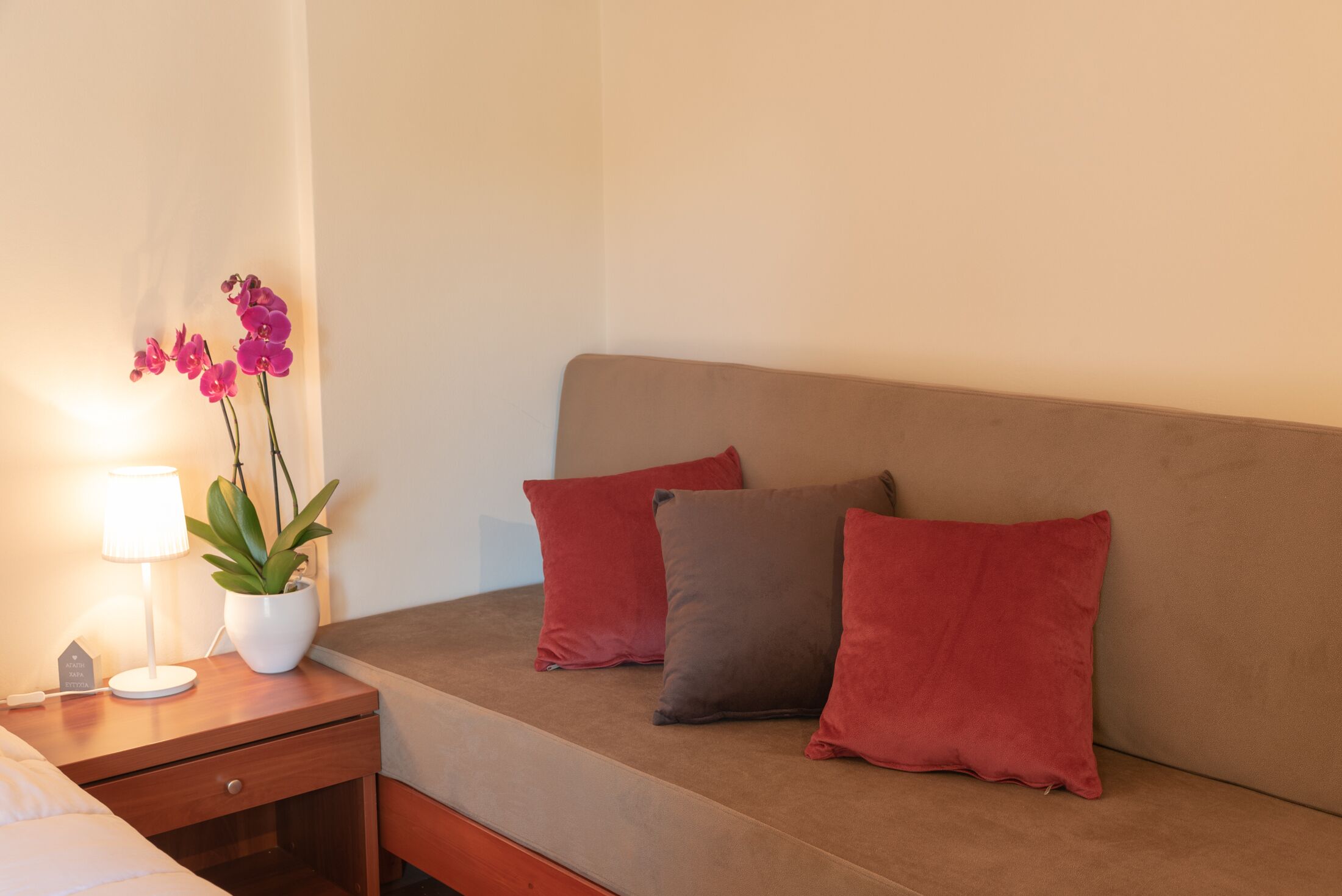 A bedroom with a bed, a bedside table with a lamp, a potted plant, and two pillows.