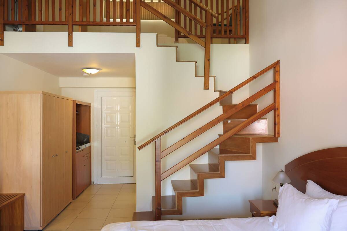 A bedroom with a wooden staircase, a bed with white bedding, and a wooden wardrobe.