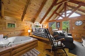 Interior acogedor de una cabaña con una cama grande, una mecedora, una bañera y techo de madera.