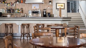 A bar area with wooden stools and tables, a coffee machine, and shelves with various bottles. - Ardora Restaurant and Hotel (Sanxenxo)