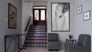 A staircase with patterned tiles, a framed artwork of a woman holding a fan, and a grey armchair in a neutral-toned room. - Ardora Restaurant and Hotel (Sanxenxo)