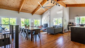 Amplia sala de estar con techo de madera, una mesa de comedor con sillas, un sofá y una cocina con un ventanal grande.