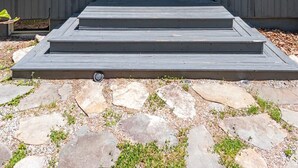 Un edificio moderno con una puerta verde, una terraza de madera y un camino de piedra.