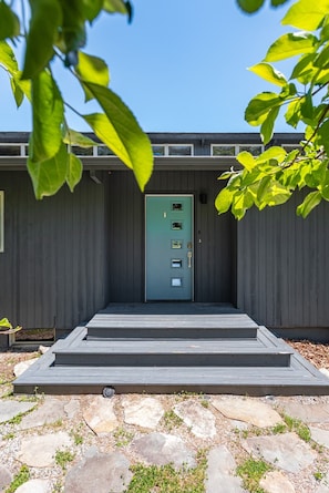Een modern gebouw met een groene deur, een houten terras en een pad van stenen.