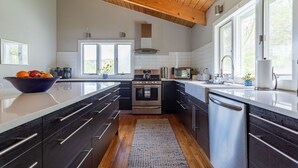 Una cocina moderna con armarios oscuros, una isla central, electrodomésticos de acero inoxidable y amplias ventanas.