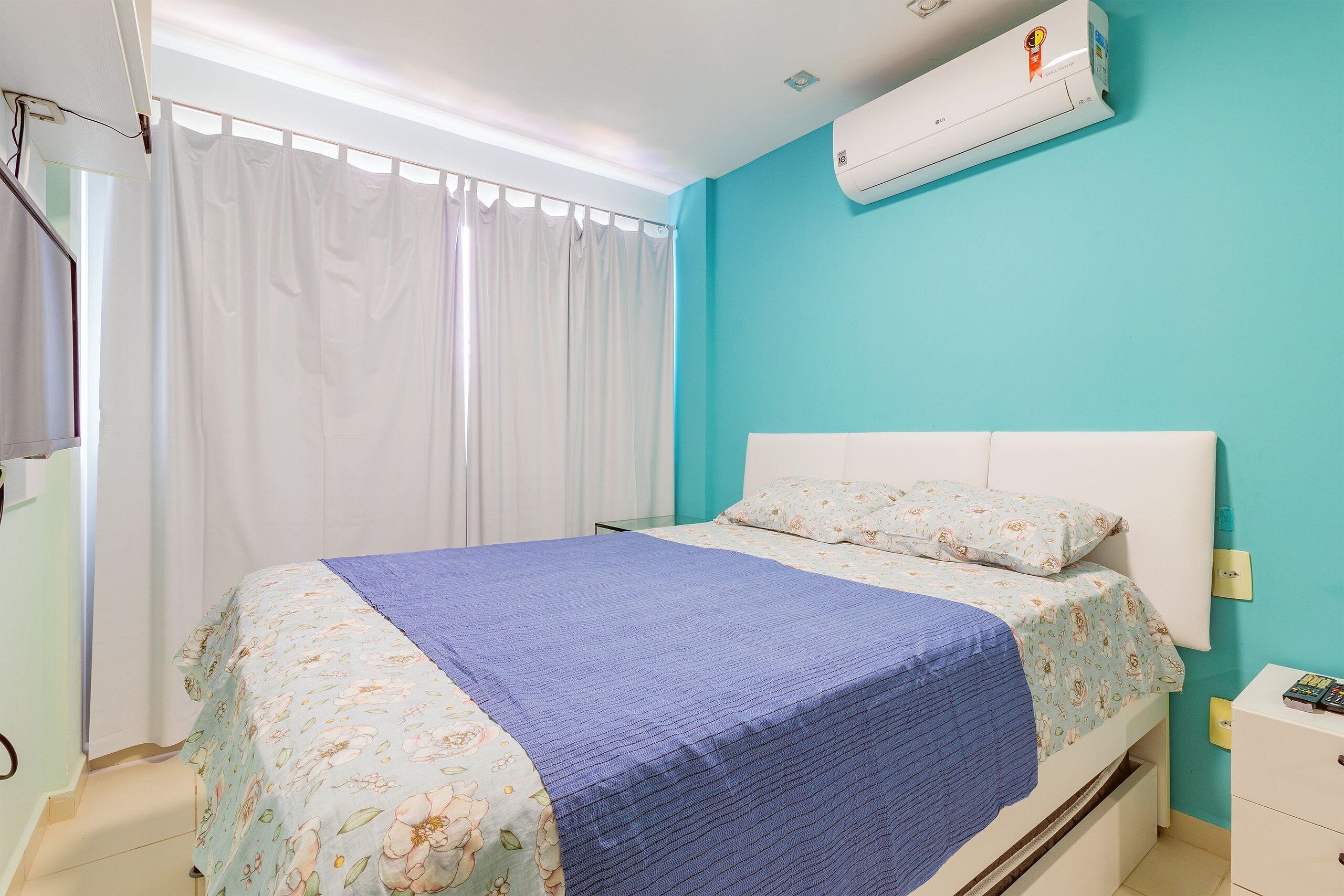 Un dormitorio con cama, mesita de noche, ventana con cortinas y aire acondicionado.
