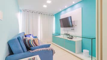 A modern living room with a blue sofa, a glass coffee table, a flat-screen TV, and a glass cabinet.