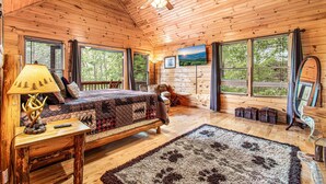 Een slaapkamer in een houten chalet met een bed, een plafondventilator, een vloerkleed en grote ramen.