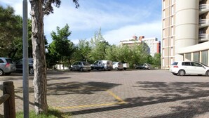 Um estacionamento com vários carros, um edifício com varandas e árvores ao fundo.
