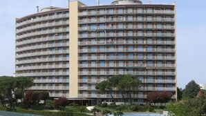 Um hotel com vários andares e fachada curva, com varandas em cada andar e uma área de piscina em primeiro plano.