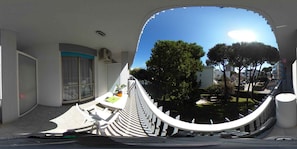 A modern room with a curved white railing, a small table with a plant, and a view of a courtyard with trees and buildings.