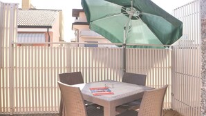 Un patio al aire libre con una mesa, sillas, un paraguas verde y una valla blanca.