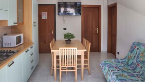 Un espacio habitable compacto con kitchenette, una mesa de comedor con sillas, un sofá y un televisor montado en la pared.