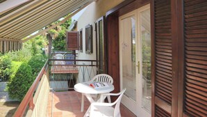 A balcony with a table and chairs, a door with a window, and a covered area with a striped awning.