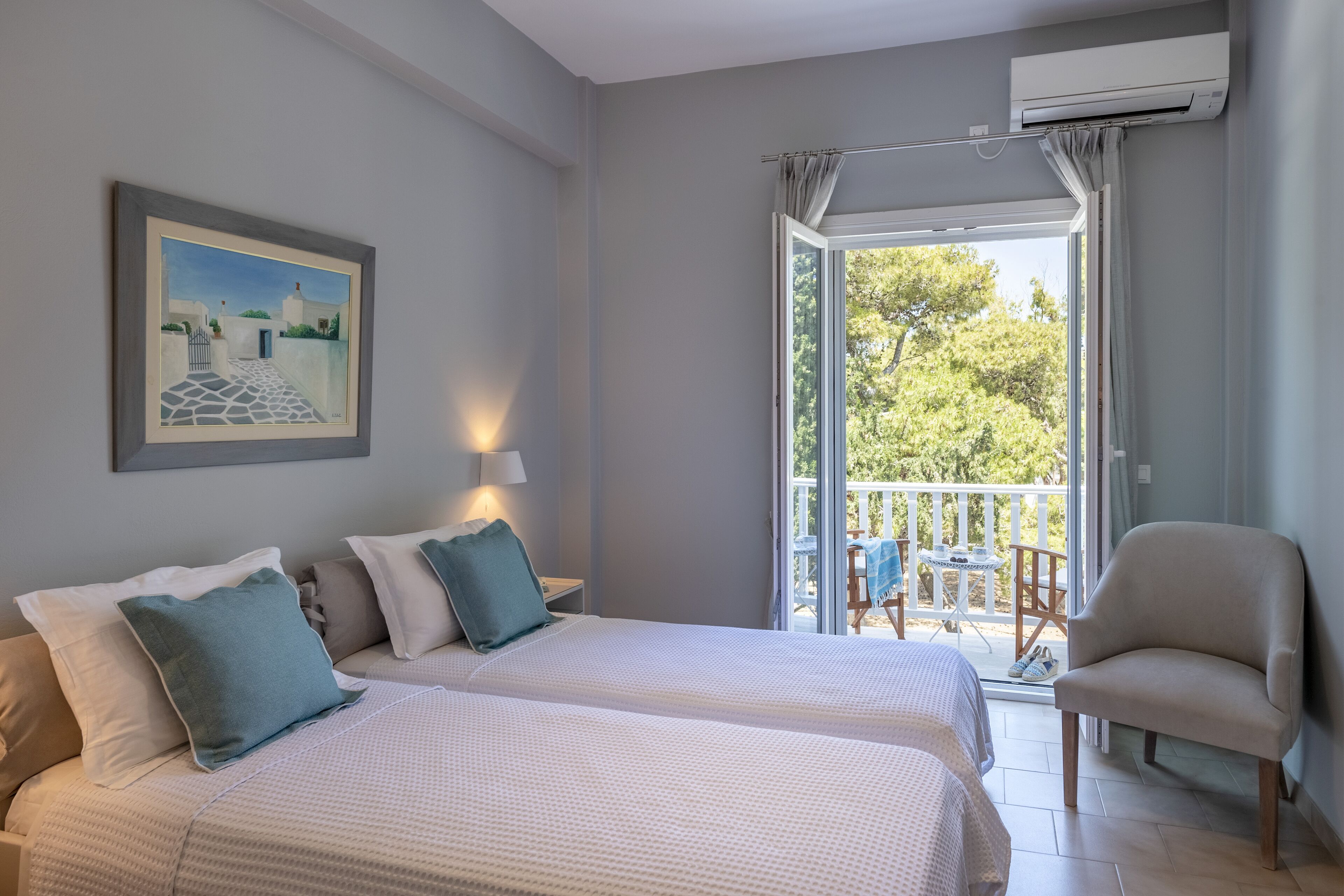 Une chambre avec deux lits, une chaise, un balcon avec une table et des chaises, et un appareil de climatisation.