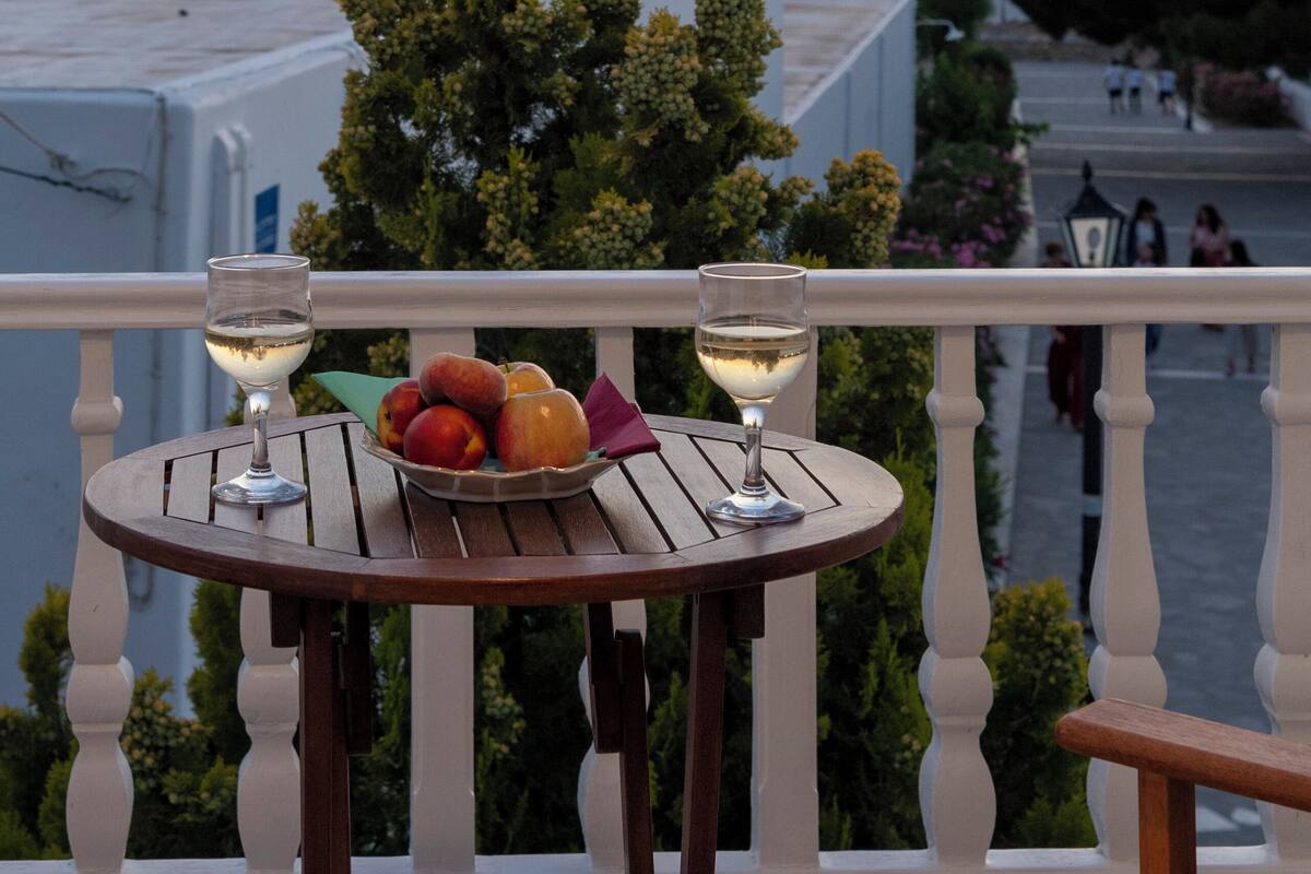 Un balcon avec une table dressée pour deux personnes, agrémenté d’un verre de vin blanc et d’un saladier de fruits.