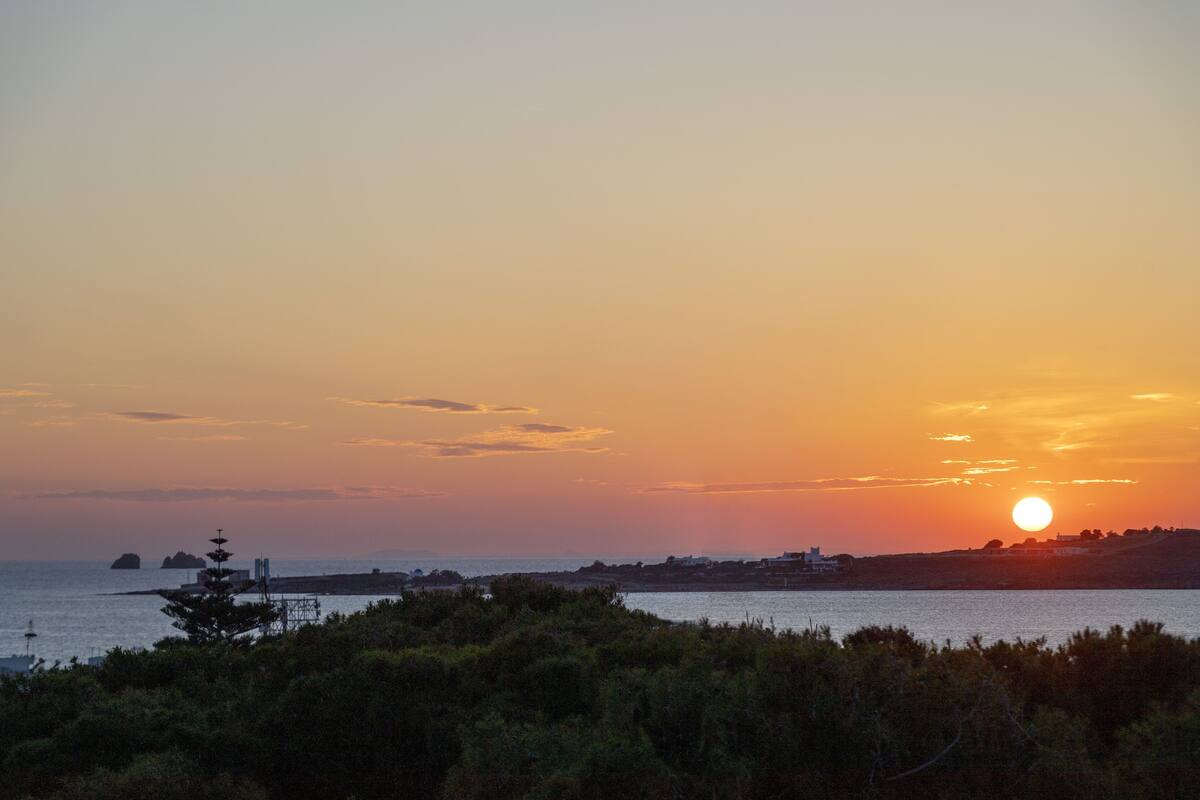 Un coucher de soleil sur un paysage côtier, avec une jetée qui s’avance dans l’eau.