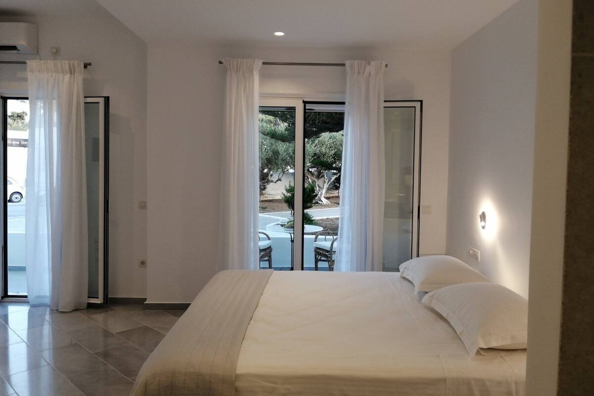 Une chambre dotée d’un grand lit et d’une porte-fenêtre coulissante donnant sur une terrasse aménagée avec du mobilier d’extérieur.