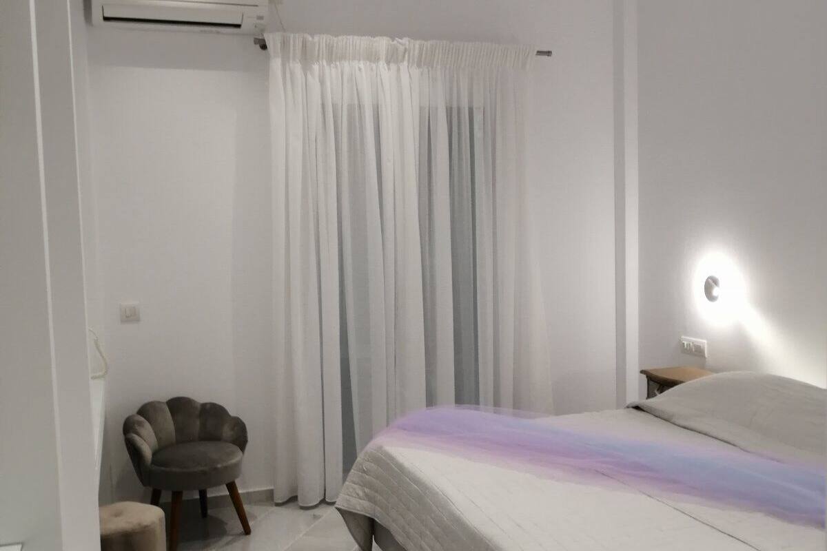 Une chambre à coucher moderne, comprenant un lit, une chaise, une table de chevet et un climatiseur fixé au mur.