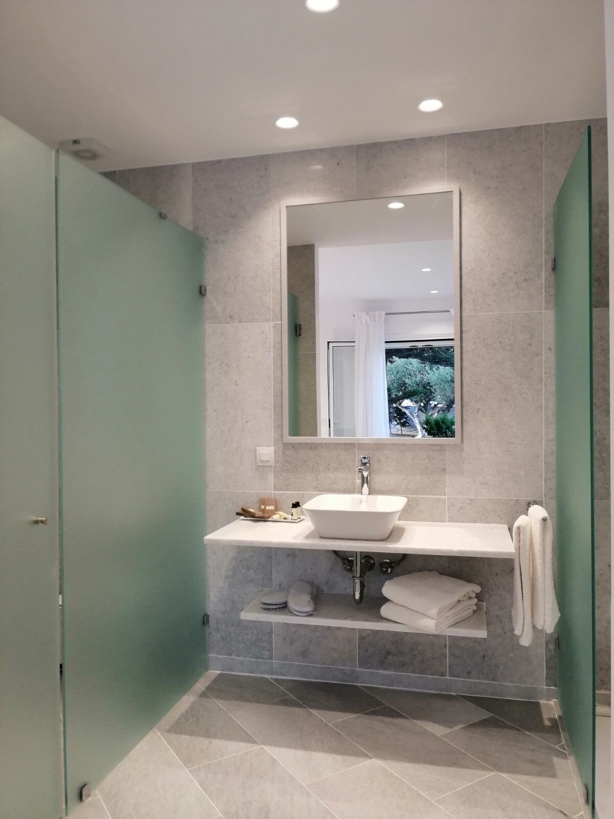 A modern bathroom with a large mirror, a white sink, and a shower area.