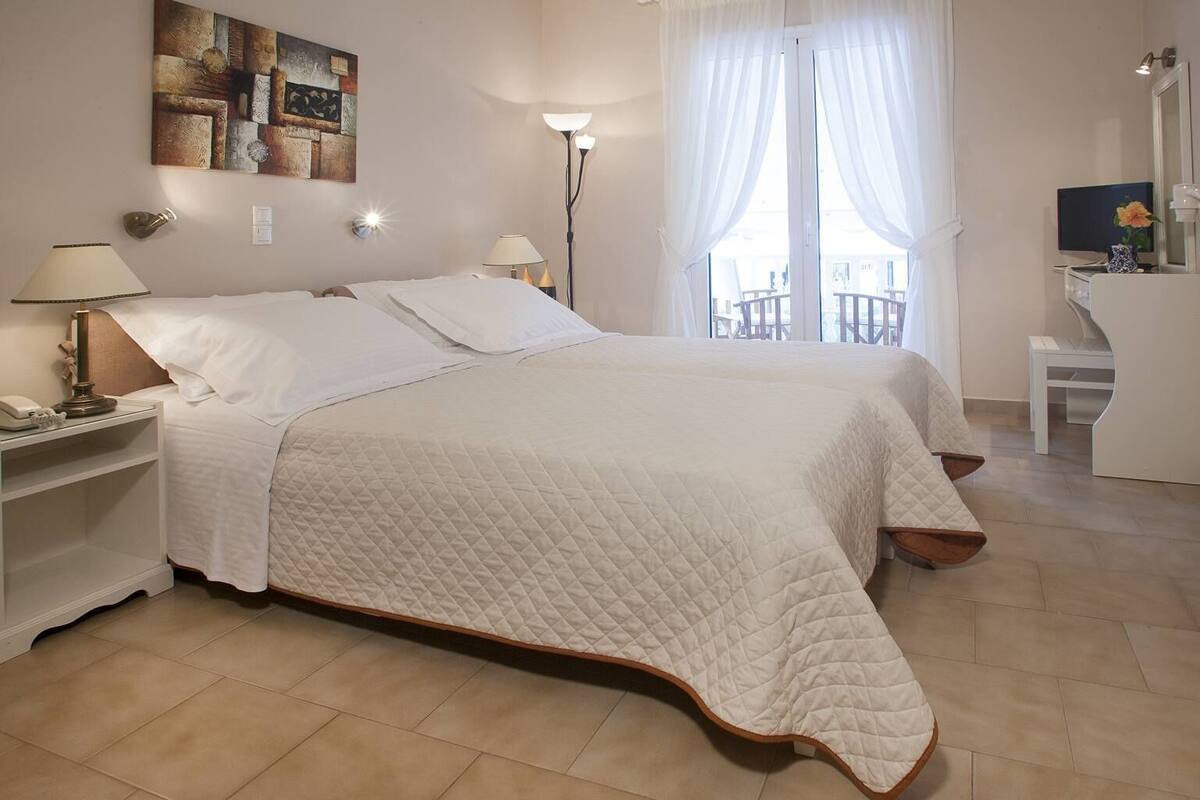 Une chambre bien éclairée, avec un grand lit, des lampes de chevet, un bureau et une chaise.