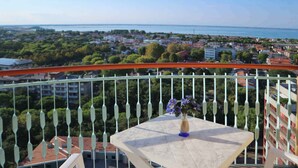 Un balcon avec une table et des chaises, donnant sur une ville côtière avec ses bâtiments et sa végétation.