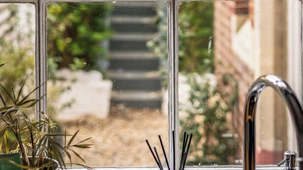 Ein Fenster mit Blick auf einen Garten, einen weißen Zaun und ein Backsteinhaus.