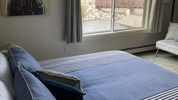 A bedroom with a large bed, a painting of a bear, a window with a view of trees and a bridge, and a chair.