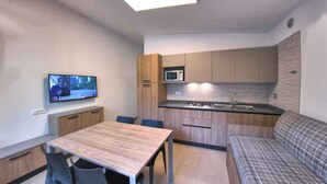 A compact kitchen with a dining area, a television, and a sofa. - Holiday apartment mit Klimaanlage und Balkon (Lignano Sabbiadoro)