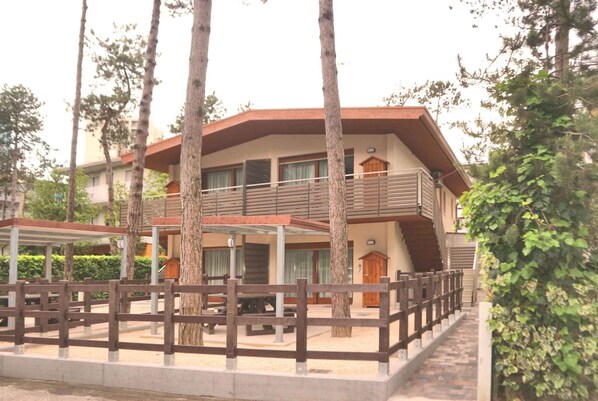 A two-story building with a balcony, surrounded by trees and a wooden fence.