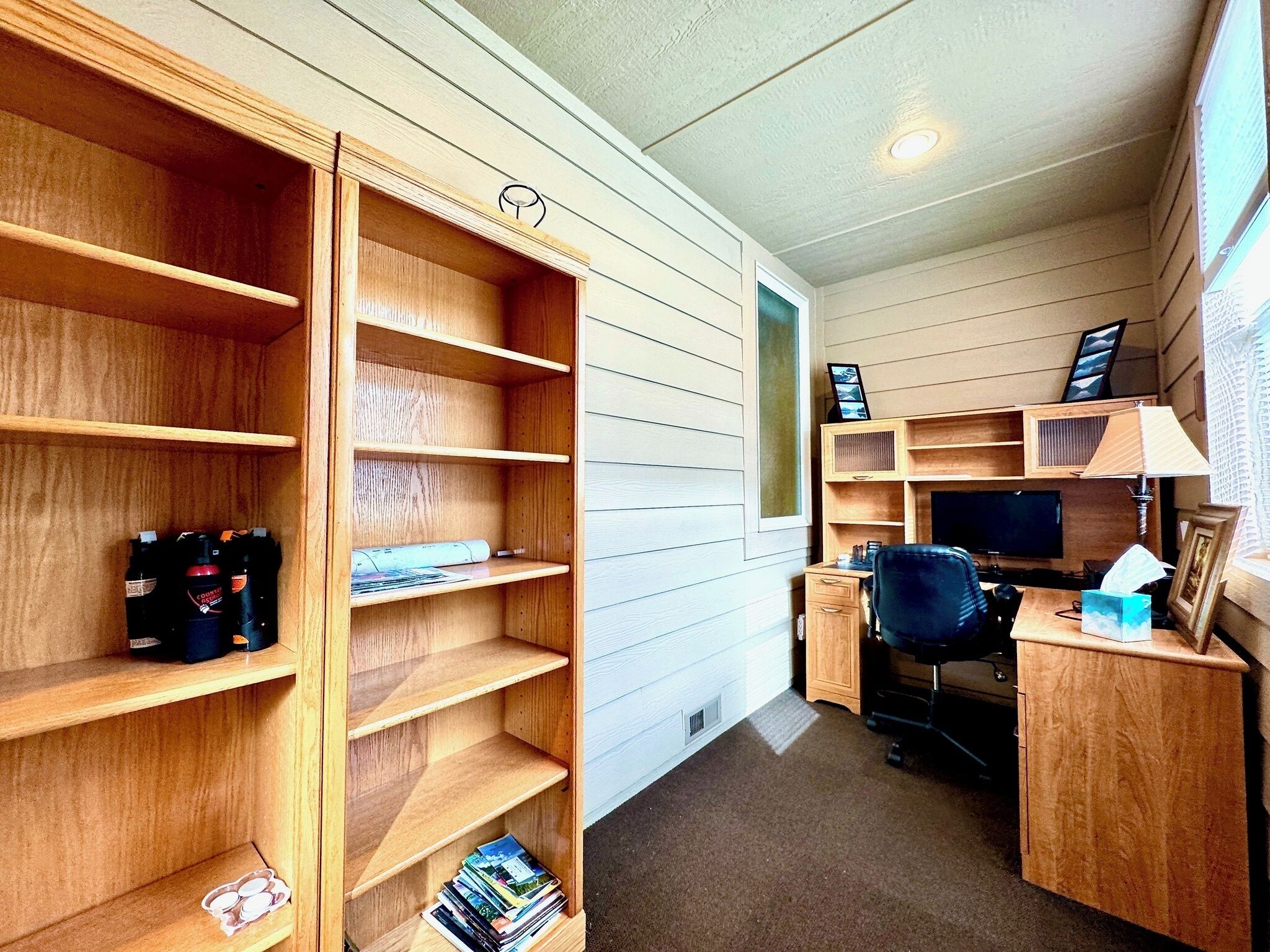A home office with wooden shelving, a desk, a chair, and a television.