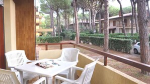 Un balcón con una mesa y cuatro sillas, con vista a un jardín con setos bien cuidados y árboles.