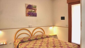 Un dormitorio con cama, mesita de noche, lámpara de pared y un cuadro enmarcado.