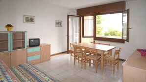 Ein Zimmer mit einem Bett, einem Holzesstisch mit Stühlen, einem Fernseher auf einer Kommode und einem Fenster mit Vorhängen.