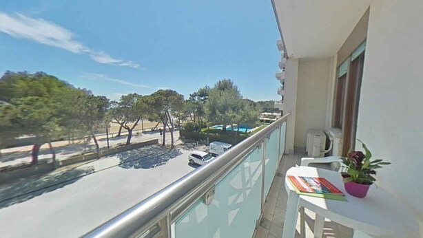 Ein Balkon mit Blick auf eine Straße, Bäume und einen Swimmingpool.