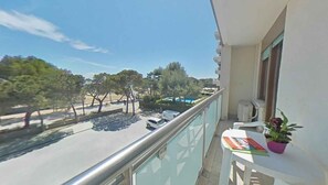 A balcony with a view of a street, trees, and a swimming pool. - Holiday apartment mit Terrasse und Meerblick (Lignano Sabbiadoro)