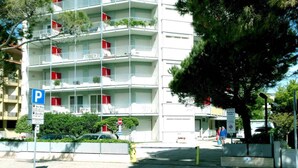 Un edificio de varios pisos con balcones, un letrero de estacionamiento y un árbol en primer plano.