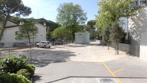 Un área de estacionamiento pavimentada con un pequeño cobertizo, rodeado de árboles y edificios.