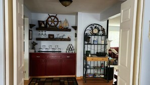 Un pasillo con piso de madera, un tapete estampado, un reloj y una repisa con objetos decorativos.