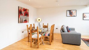 Ein modernes Wohnzimmer mit Esstisch, grauem Sofa und Bildern an den Wänden.
