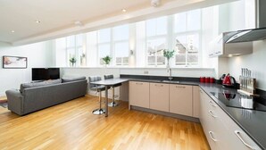 Eine moderne Küche mit Essbereich, großen Fenstern und einem grauen Sofa im Wohnzimmer.