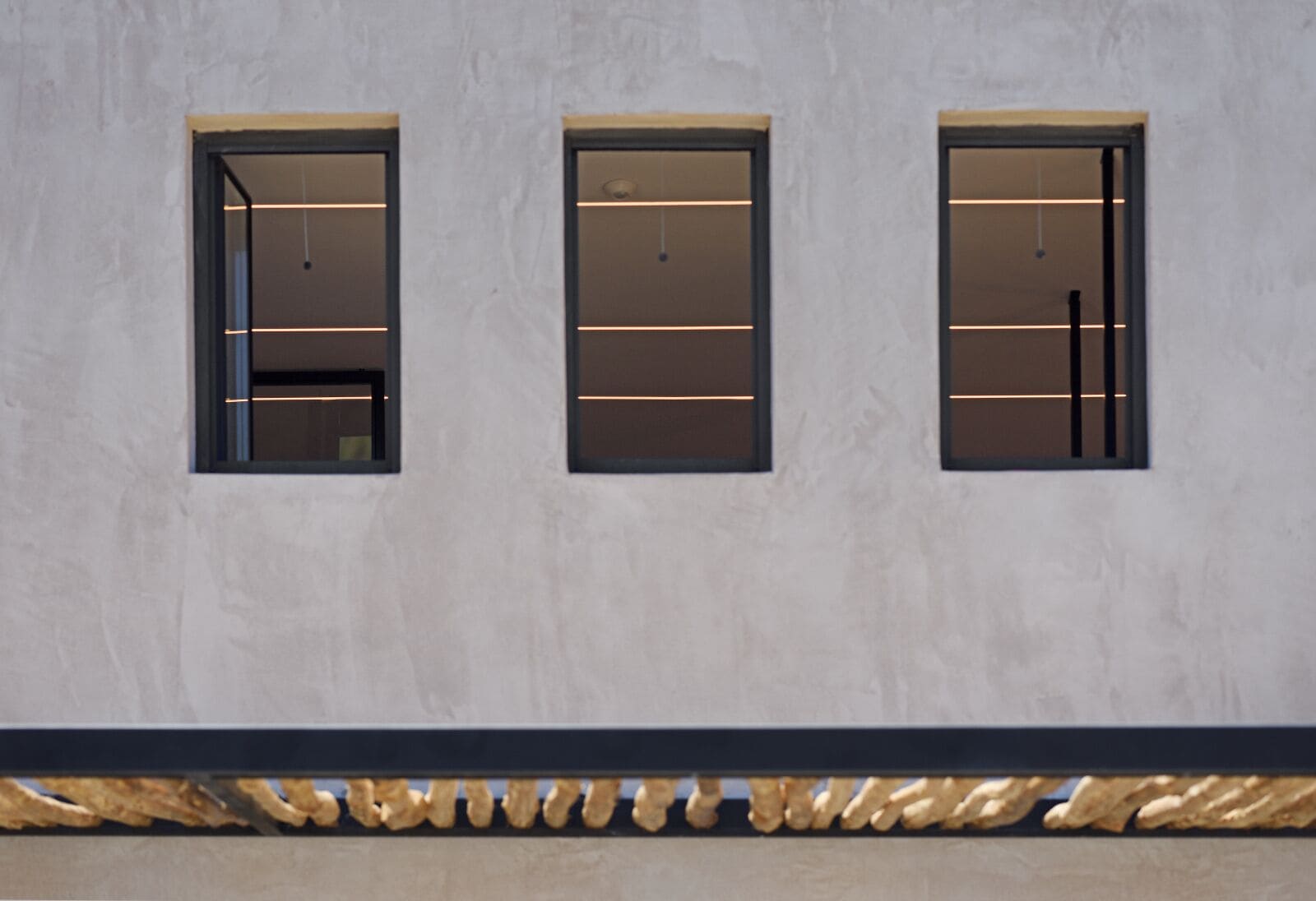 Three windows with horizontal light strips, a textured wall, and a decorative golden trim.