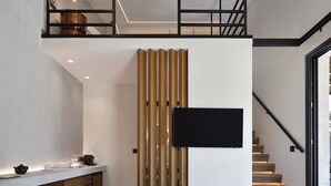 A modern kitchen with a white countertop, wooden cabinets, and a black flat-screen TV mounted on a wooden panel. - Pure Villas (Sithonia)