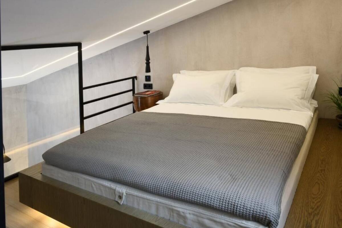 A modern bedroom with a bed, a nightstand, a lamp, and a view of the sky.
