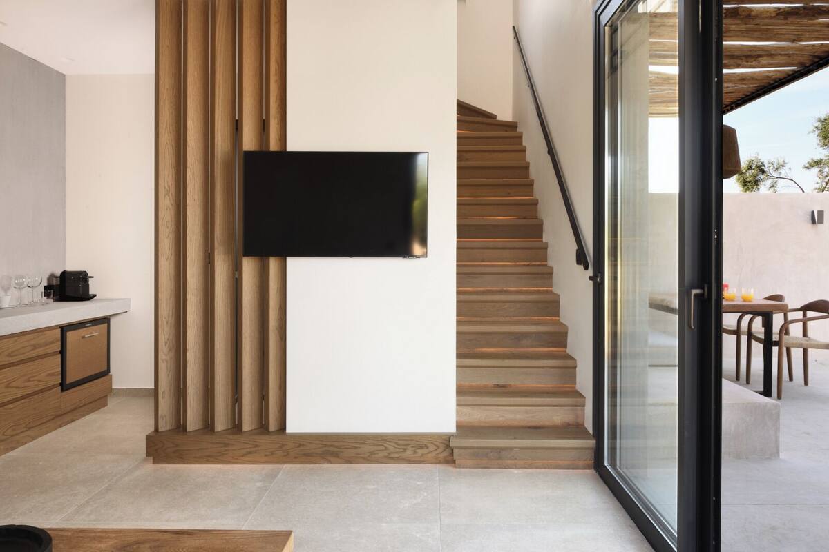 A modern kitchen with wooden cabinetry, a flat-screen TV mounted on the wall, and a staircase leading to an outdoor seating area.