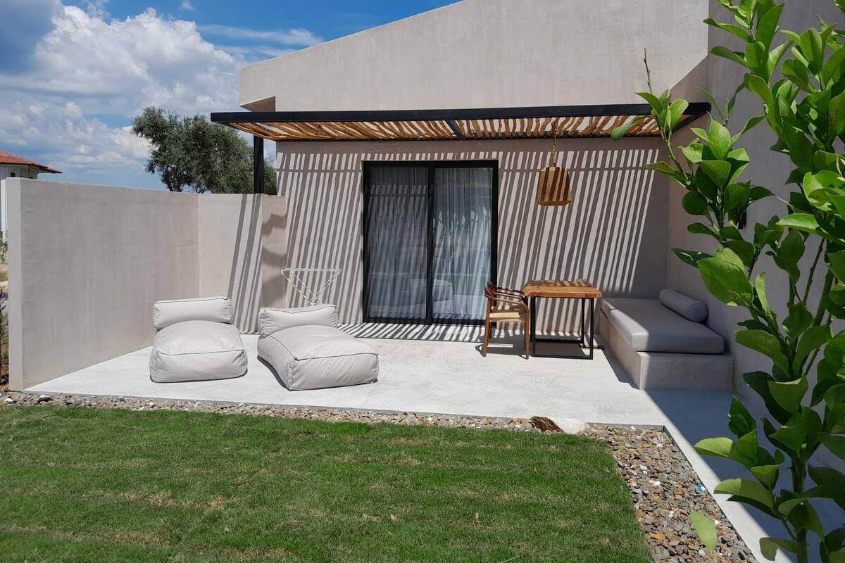 A modern outdoor seating area with a pergola, cushioned seating, and a small table.