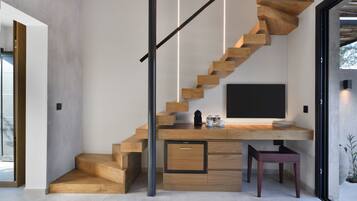 Una escalera moderna con escalones de madera y barandilla negra, que lleva a un espacio de trabajo con una televisión de pantalla plana, una cafetera y un taburete pequeño.