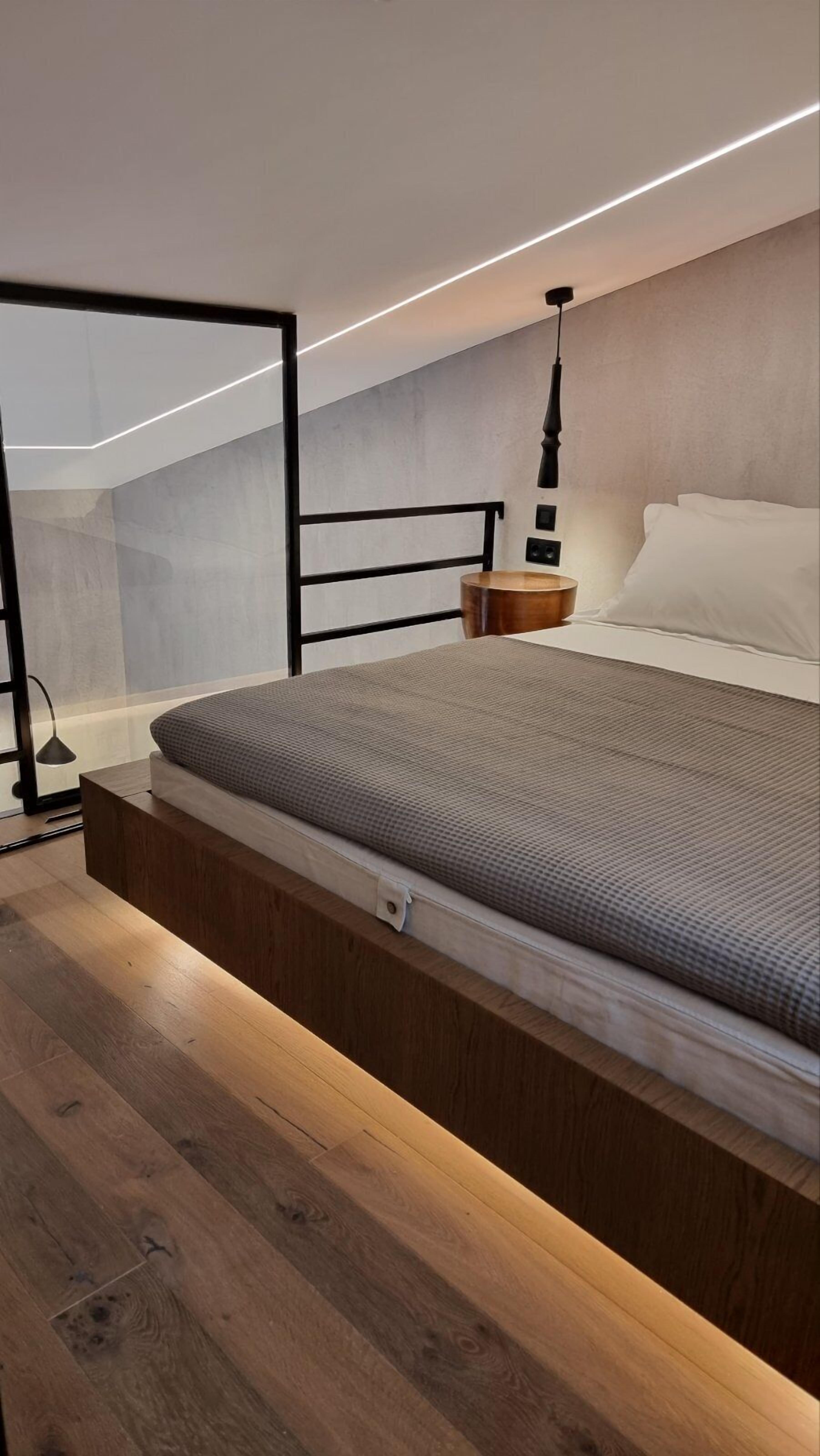 A modern bedroom with a built-in bed, wooden flooring, a bedside table, and a wall-mounted light fixture.