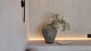 A corner seating area with a textured wall, a stone vase with a plant, and a black wall-mounted lamp. - Pure Villas (Sithonia)